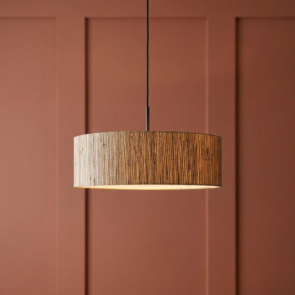 Drum-shaped seagrass pendant light hanging against a terra cotta paneled wall.