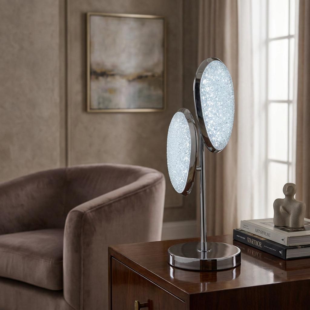 Modern table lamp with two oval crushed-ice LED shades and chrome finish, sitting on a wooden side table.