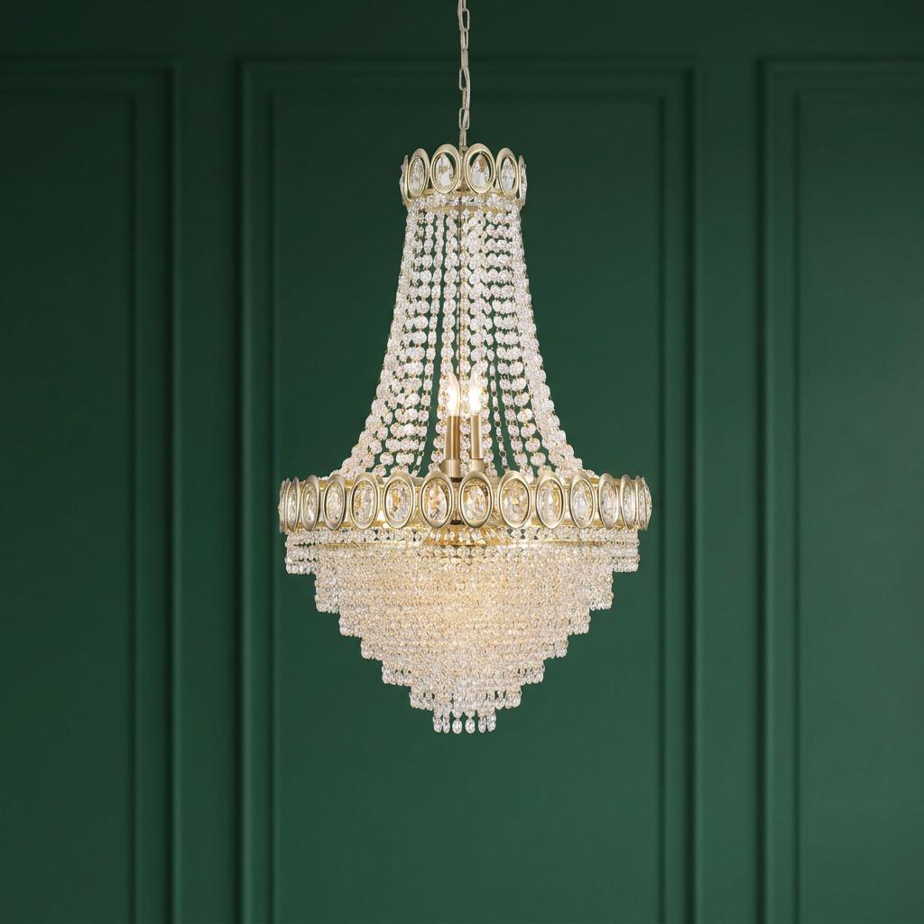 A tiered Louis Phillipe crystal chandelier with a satin brass frame, hanging against a dark green paneled wall.