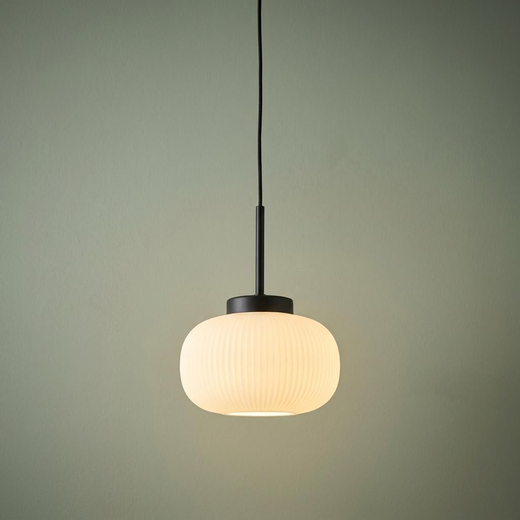Lumina 1 light pendant with a frosted ribbed glass shade and black fixture against a light green wall.