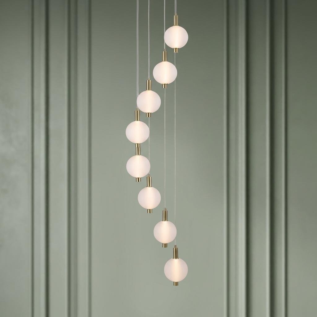 Eight-globe cascading pendant light with ribbed glass and satin brass fittings against a sage green paneled wall.