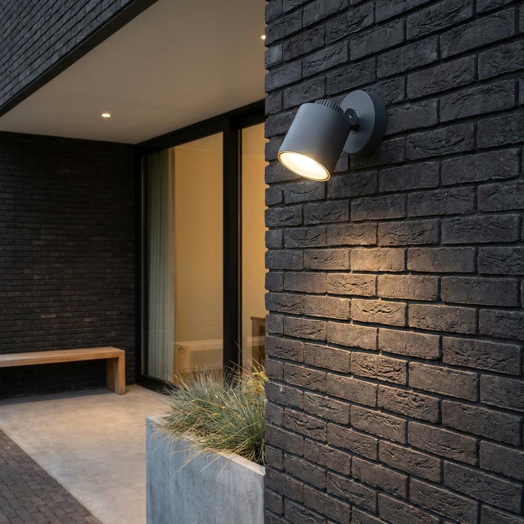 Dark grey Lutec Explorer outdoor LED wall light illuminated on a dark brick wall.