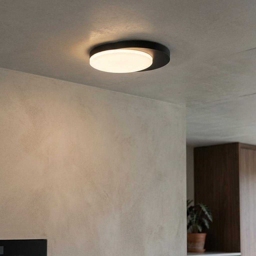 Round matt black LED flush ceiling light with a glowing white diffuser on a textured concrete surface.