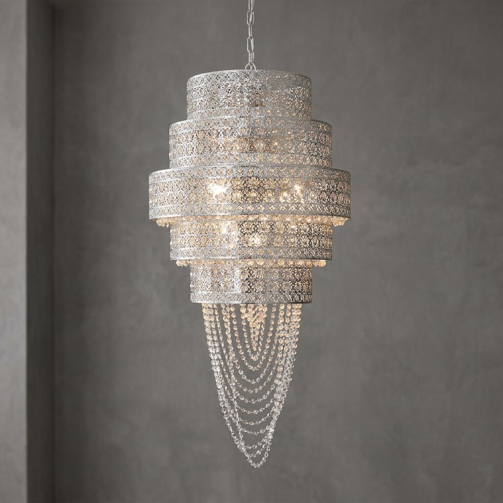 Intricate tiered chrome chandelier with perforated metal patterns and cascading crystal beads against a grey wall.
