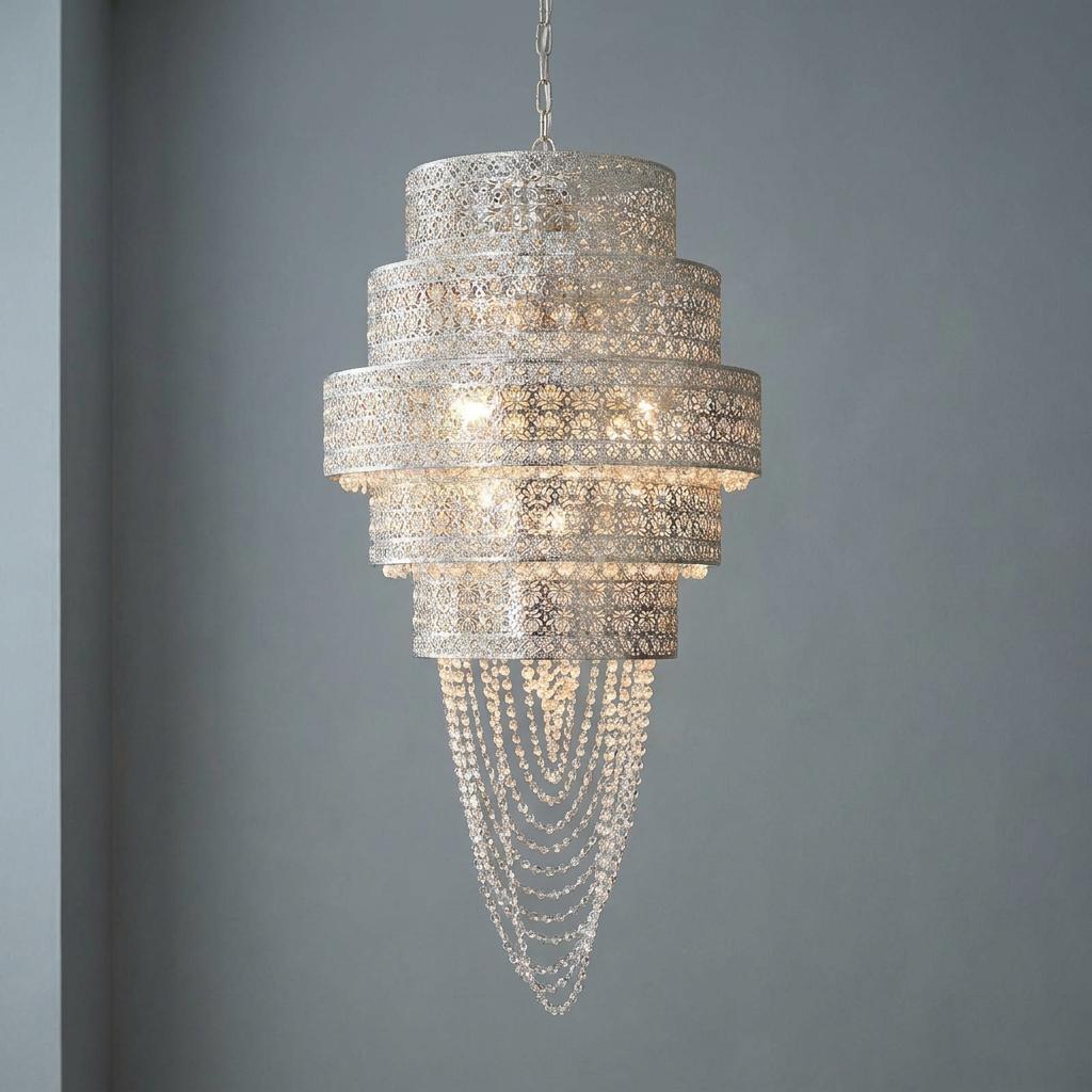 Ornate tiered chrome chandelier with perforated metal patterns and cascading crystal beads against a grey wall.