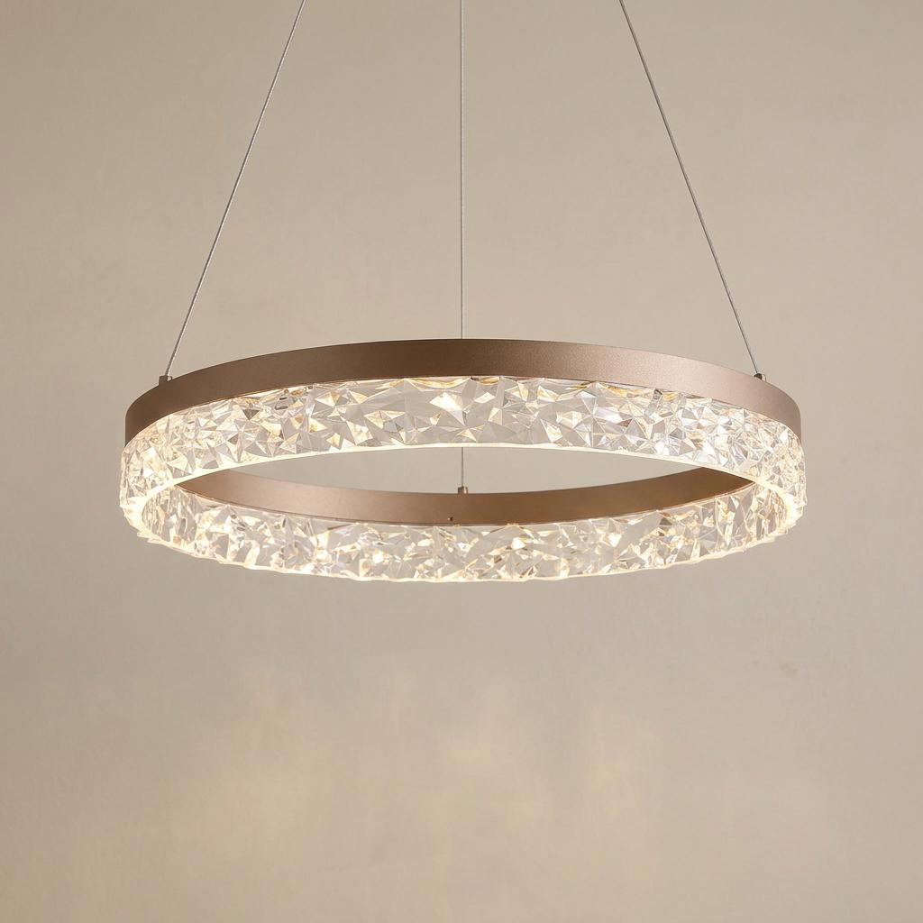 Maddie LED round pendant in latte metal with glowing faceted crystal details suspended against a neutral wall.