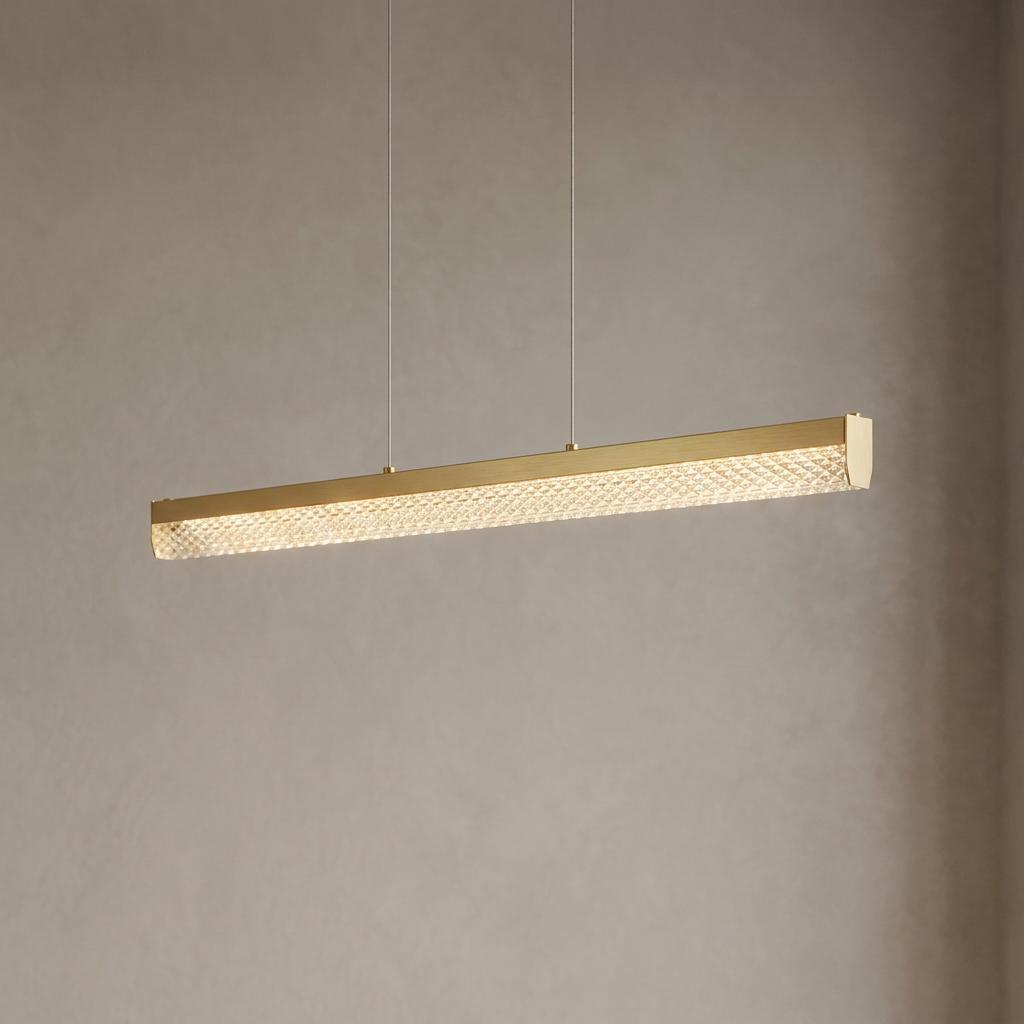 Linear matt gold pendant light with an illuminated textured crystal panel, suspended against a neutral wall.