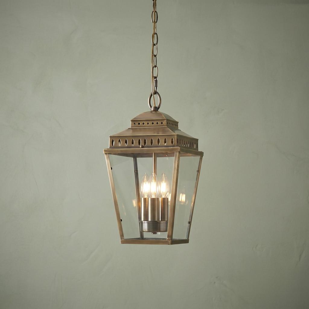 Traditional brass 3-light outdoor chain lantern with clear glass panes hanging against a textured wall.