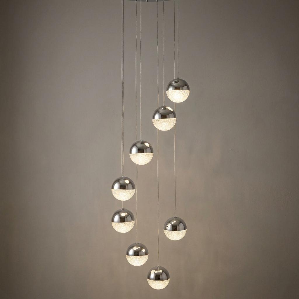Eight chrome and crackled acrylic globe pendants hanging at staggered heights against a plain wall.