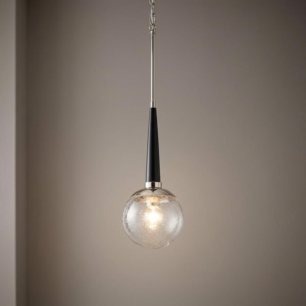 Polished nickel pendant light with a black tapered neck and a seeded glass globe shade against a neutral wall.