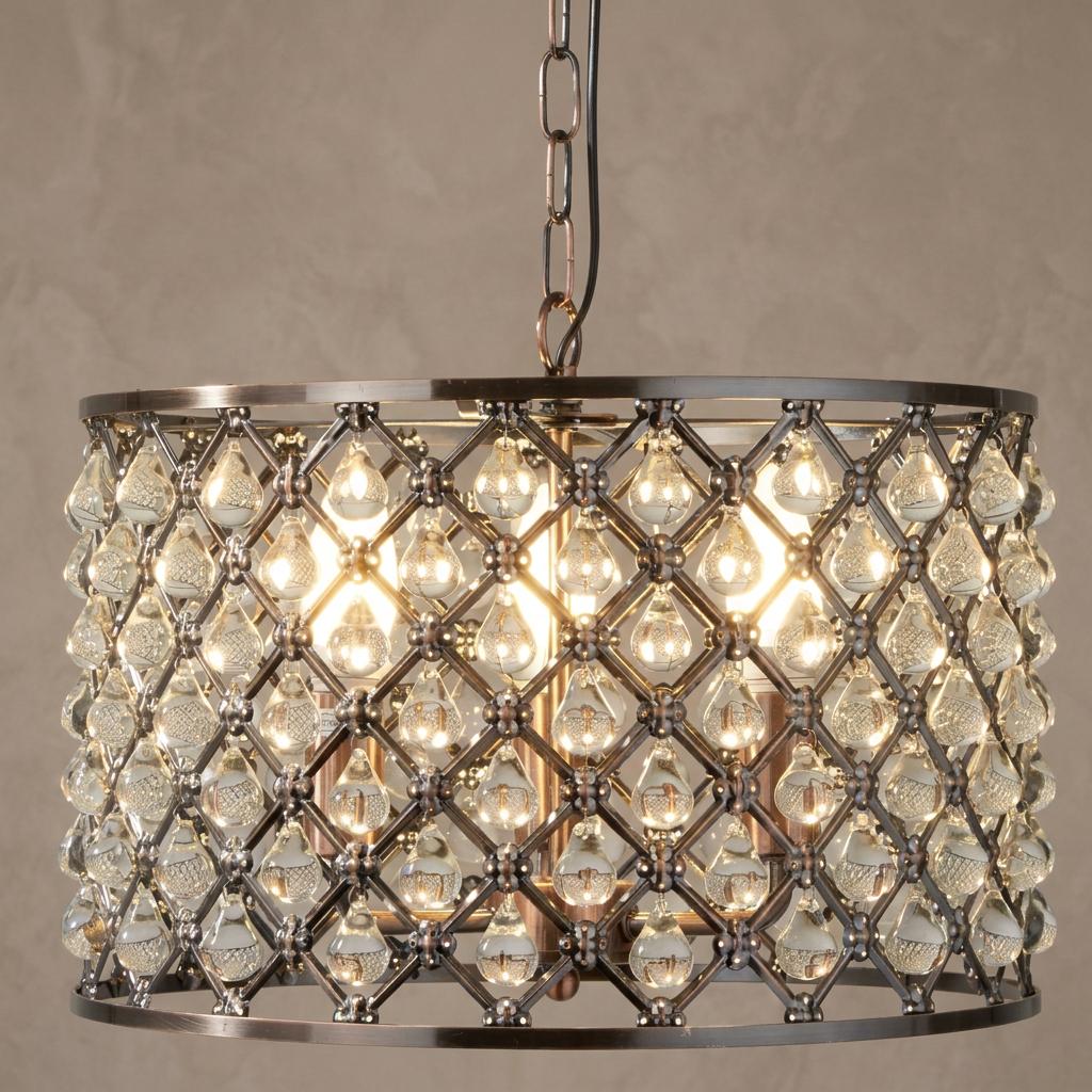 A copper drum pendant featuring a lattice frame and crystal teardrop accents, lit from within against a plain wall.