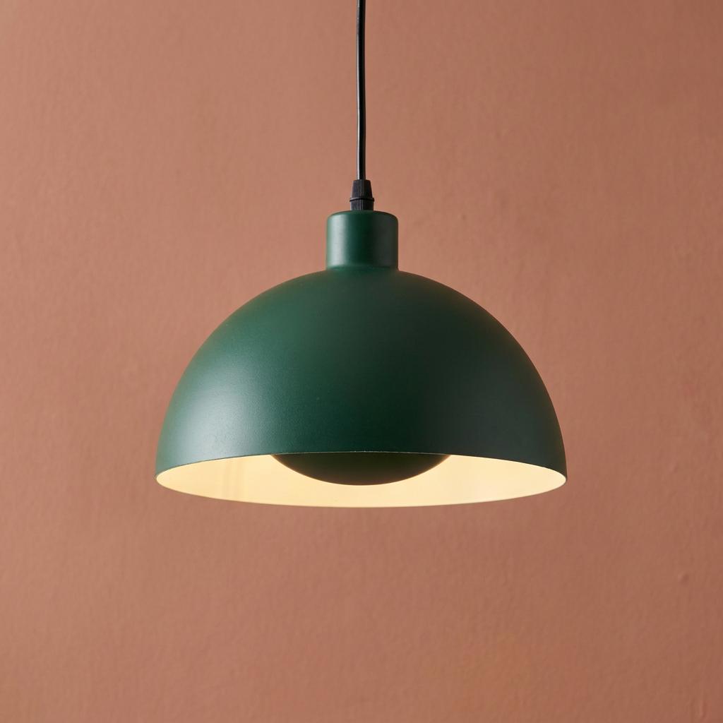 A matt green dome pendant light with a cream interior hangs against a textured peach wall.