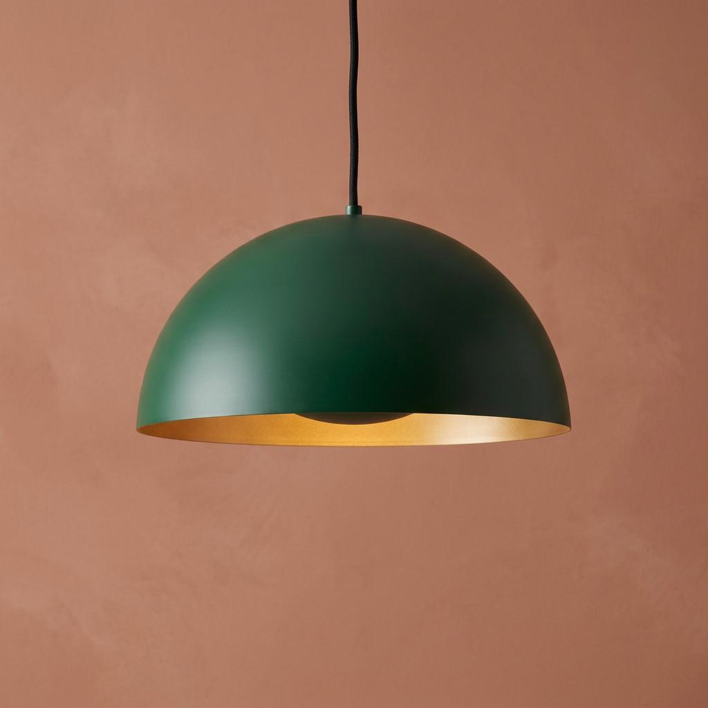 Matt green dome pendant light with a cream interior hanging against a textured terracotta wall.