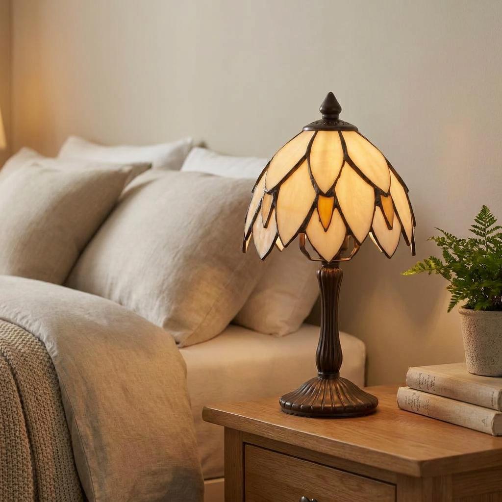 Cream petal-shaped Tiffany bedside lamp on a wooden nightstand in a warm bedroom setting.