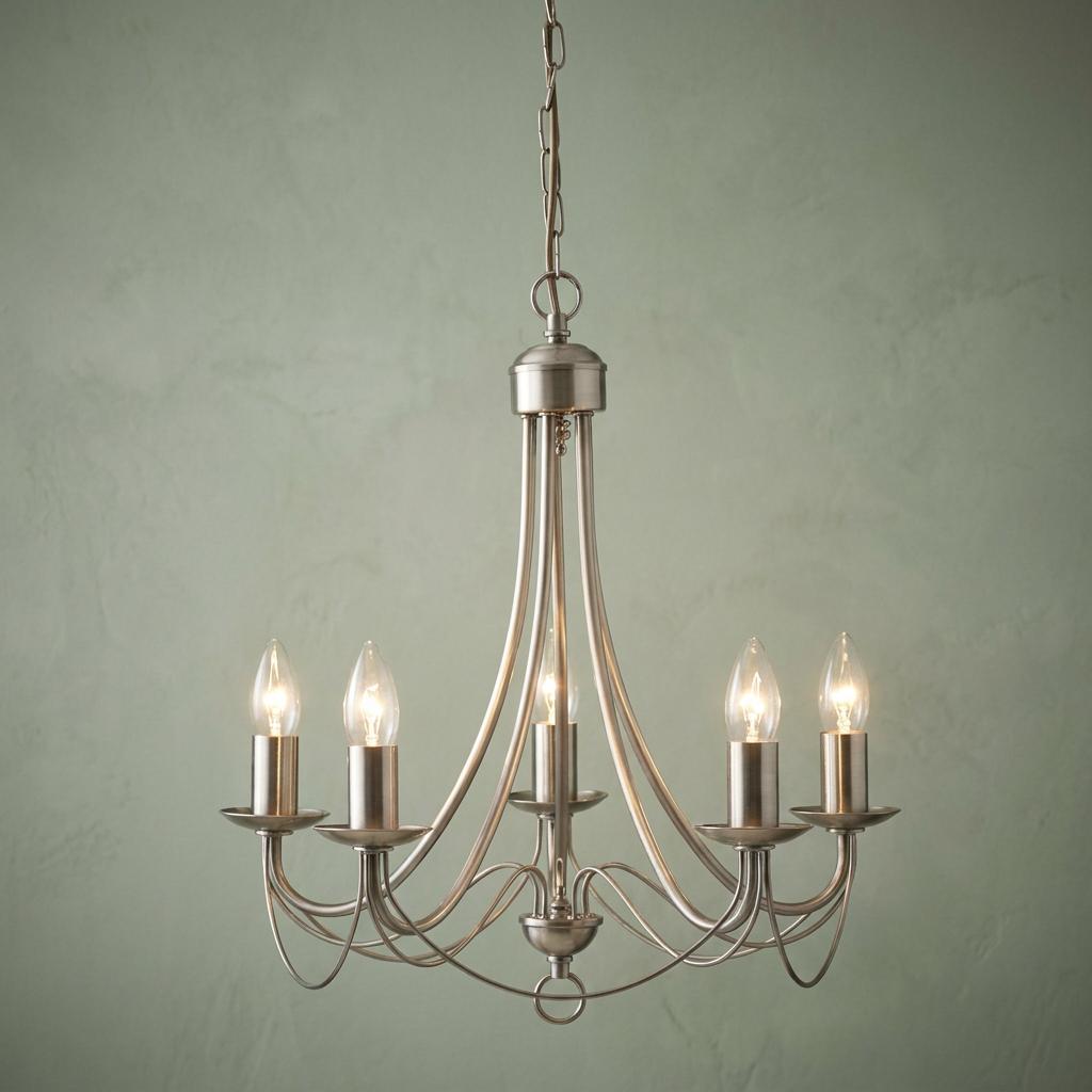 Elegant 5-light satin silver chandelier with lit candle bulbs against a pale green textured wall.