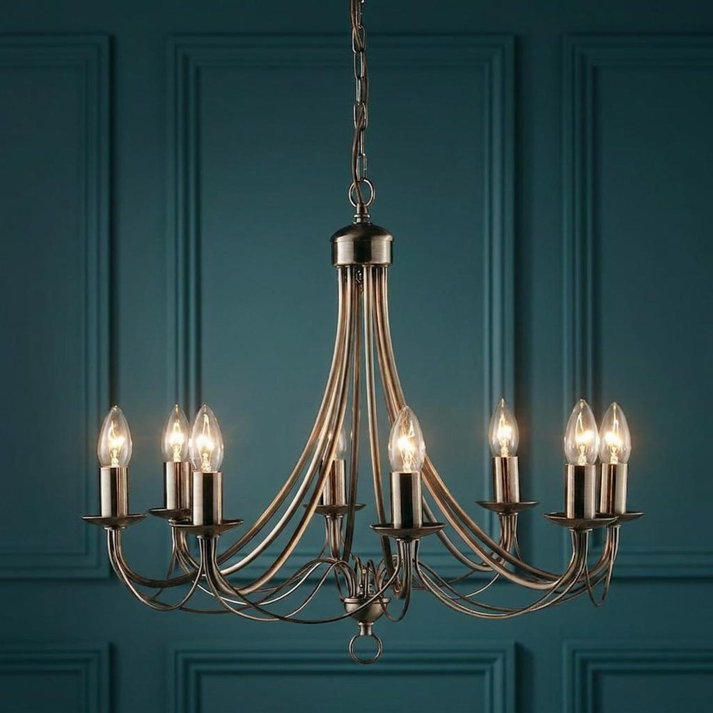 An 8-light antique brass ceiling pendant with glowing candle-style bulbs against a teal paneled wall.