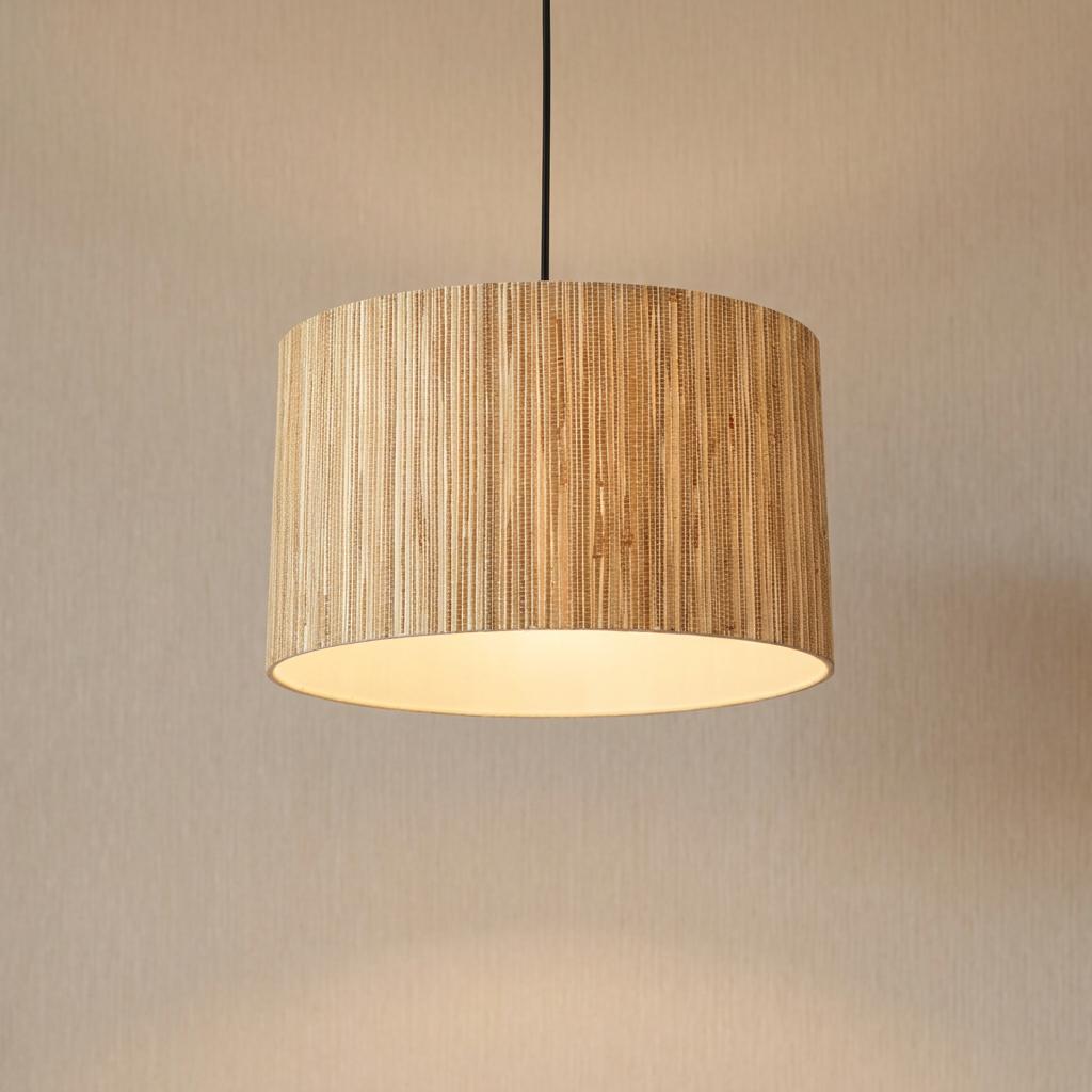 Natural grass drum pendant light with a warm glow hanging against a textured neutral wall.