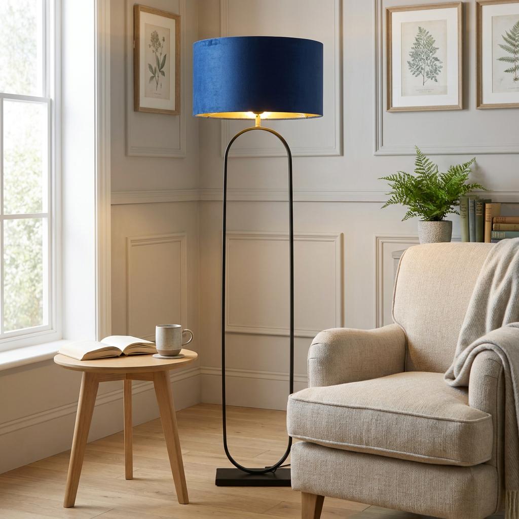 Matt black floor lamp with a navy velvet shade standing next to a beige armchair in a modern living room.