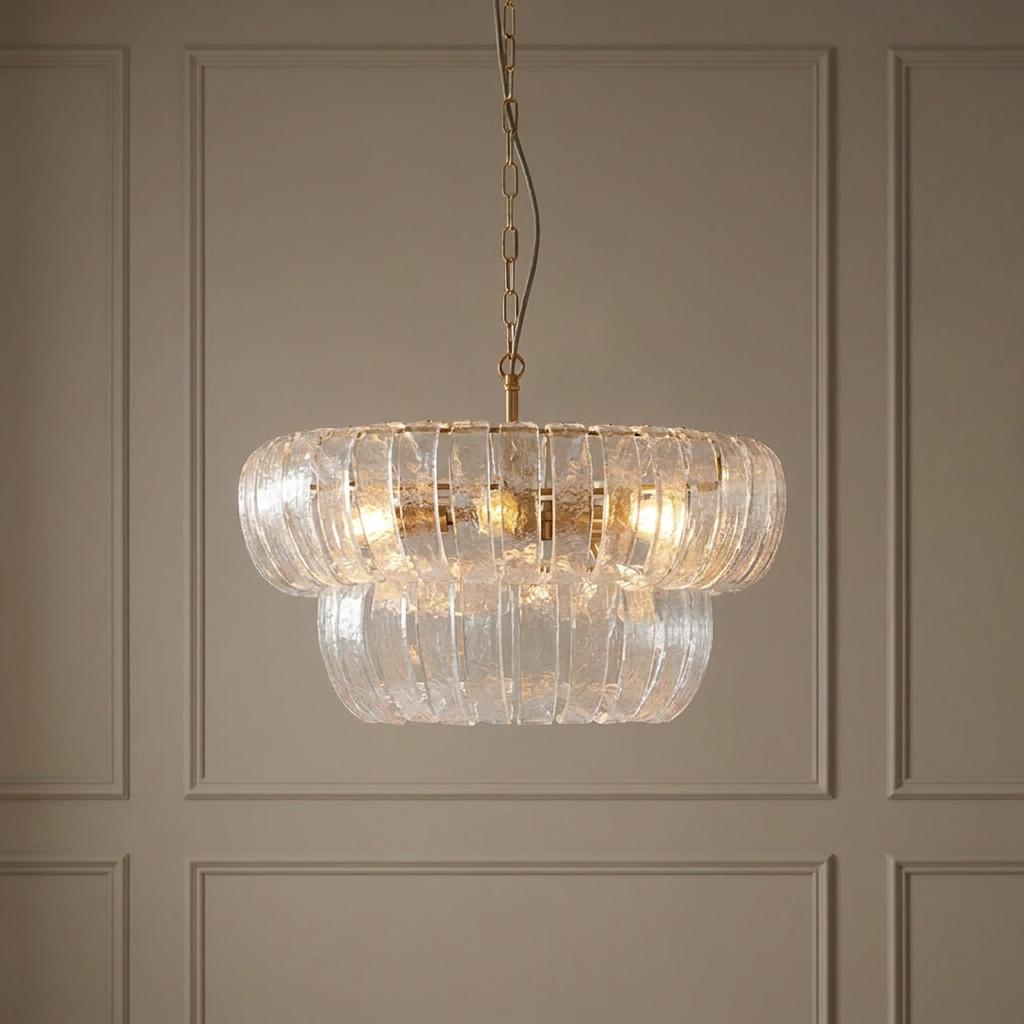 Two-tiered brass pendant light with curved textured glass panels hanging against a beige paneled wall.