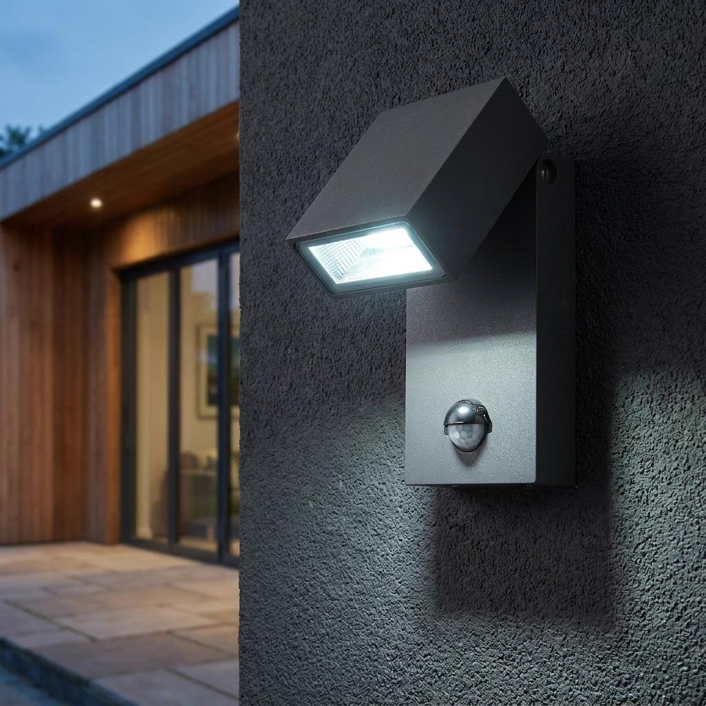 Modern grey outdoor wall light with a PIR sensor illuminated on a dark textured wall of a contemporary home.