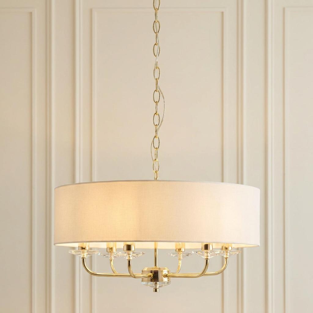 Nixon 6-light brass and glass pendant with a white drum shade against a paneled wall.