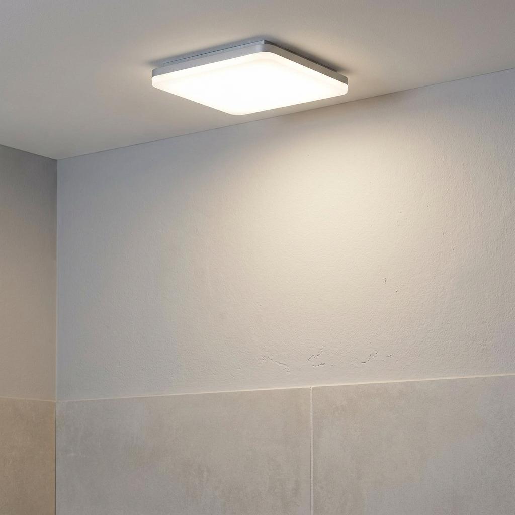 Noble White square LED flush ceiling light glowing in a tiled bathroom setting.