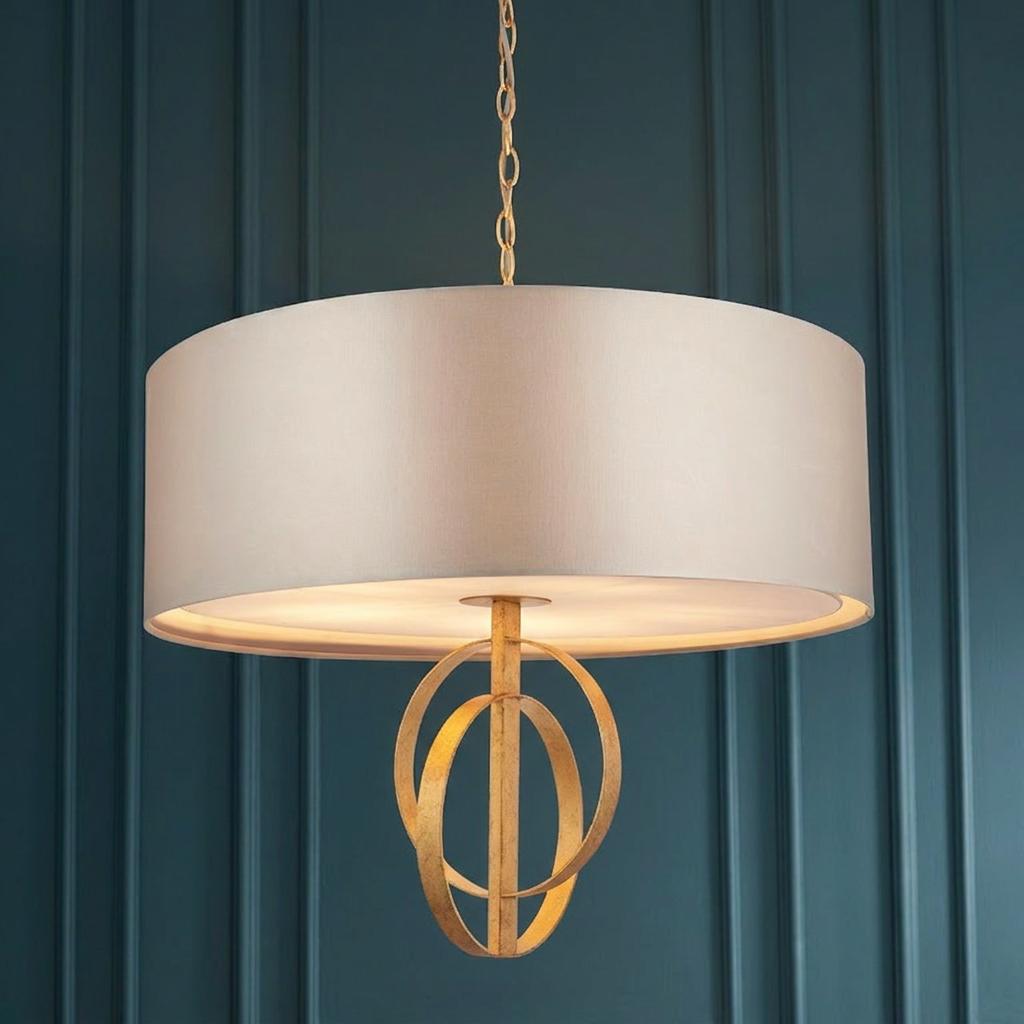 Extra large pendant light with a mink drum shade and gold leaf orbital detail against a dark teal paneled wall.