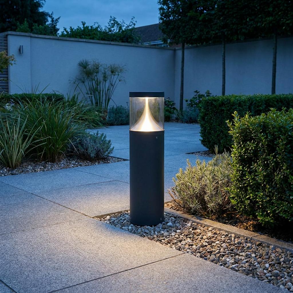 Modern graphite bollard light illuminates a stone garden path at dusk with a warm internal glow.
