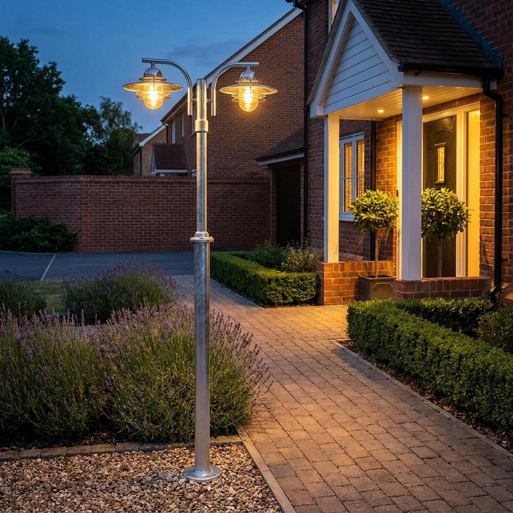 Norlys Oslo double-headed galvanized steel lamp post illuminating a brick pathway in a garden at dusk.