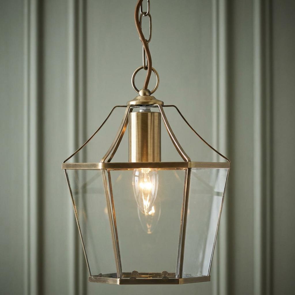 Oaks Dulverton brass ceiling lantern with clear glass panels and a glowing bulb against a paneled wall.