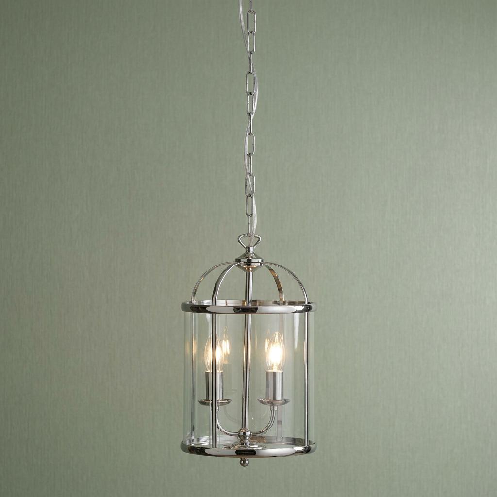 A 2-light chrome cylindrical lantern with clear glass panels hanging from a chain against a sage green wall.