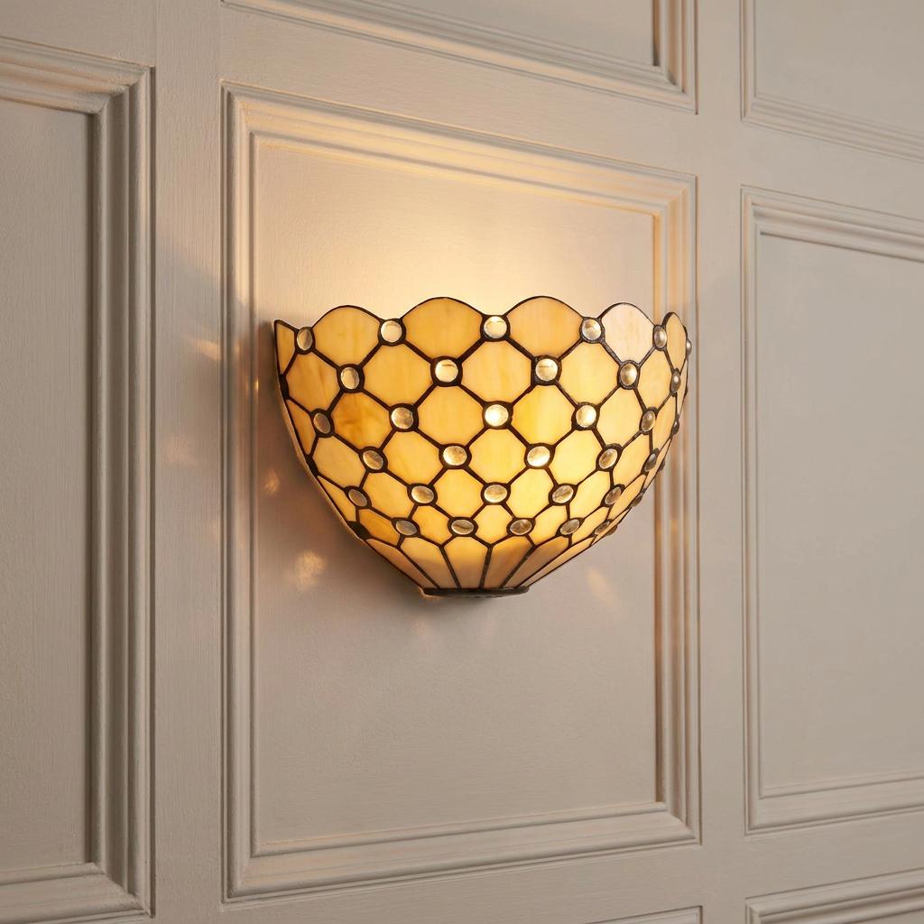 Honey-colored Tiffany wall light with a jeweled lattice pattern and scalloped edge on a paneled wall.