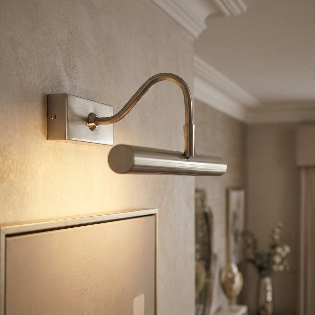 Antique chrome LED picture light with a curved arm illuminating a framed artwork on a textured wall.