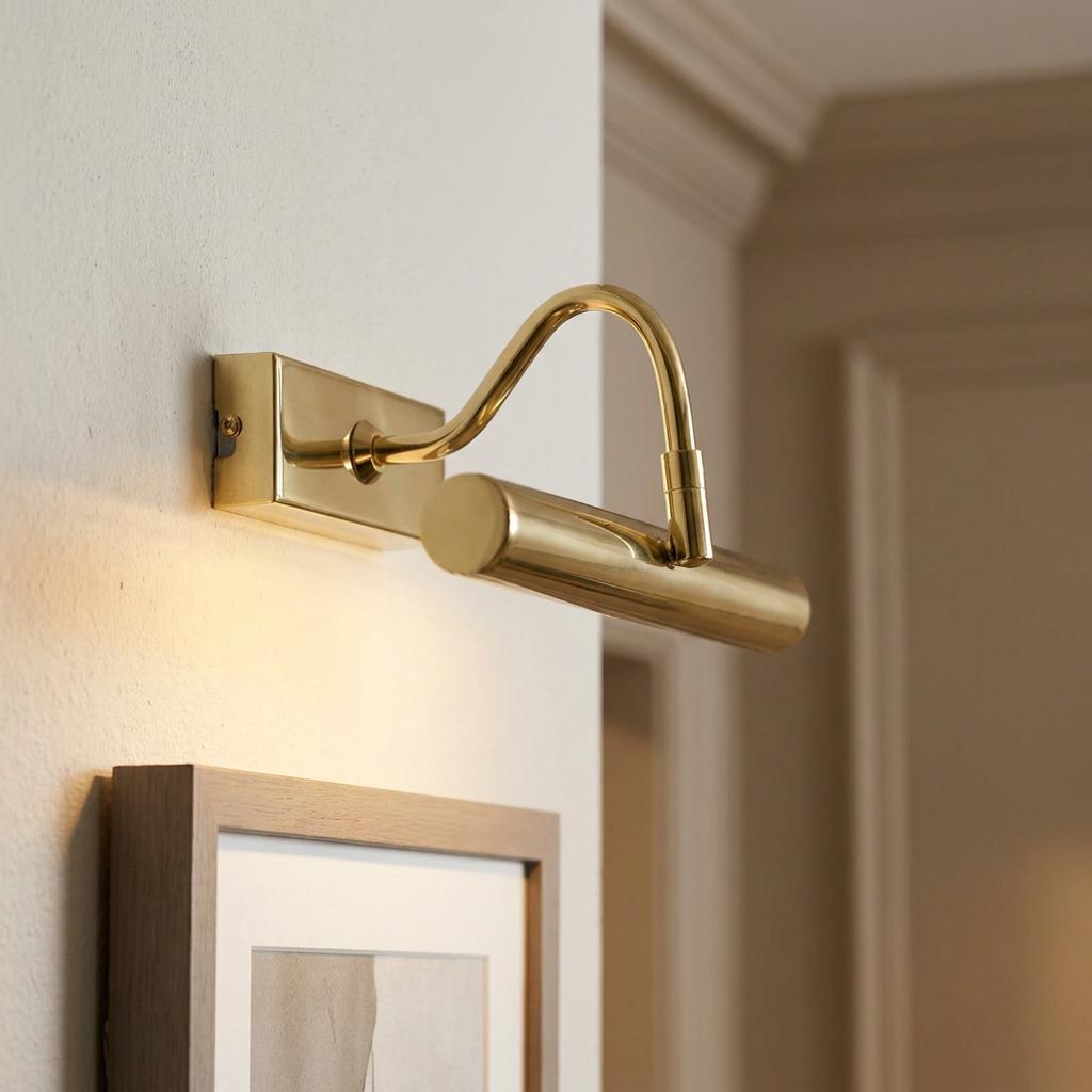 Polished brass LED picture light with a curved arm mounted on a white wall above a framed picture.
