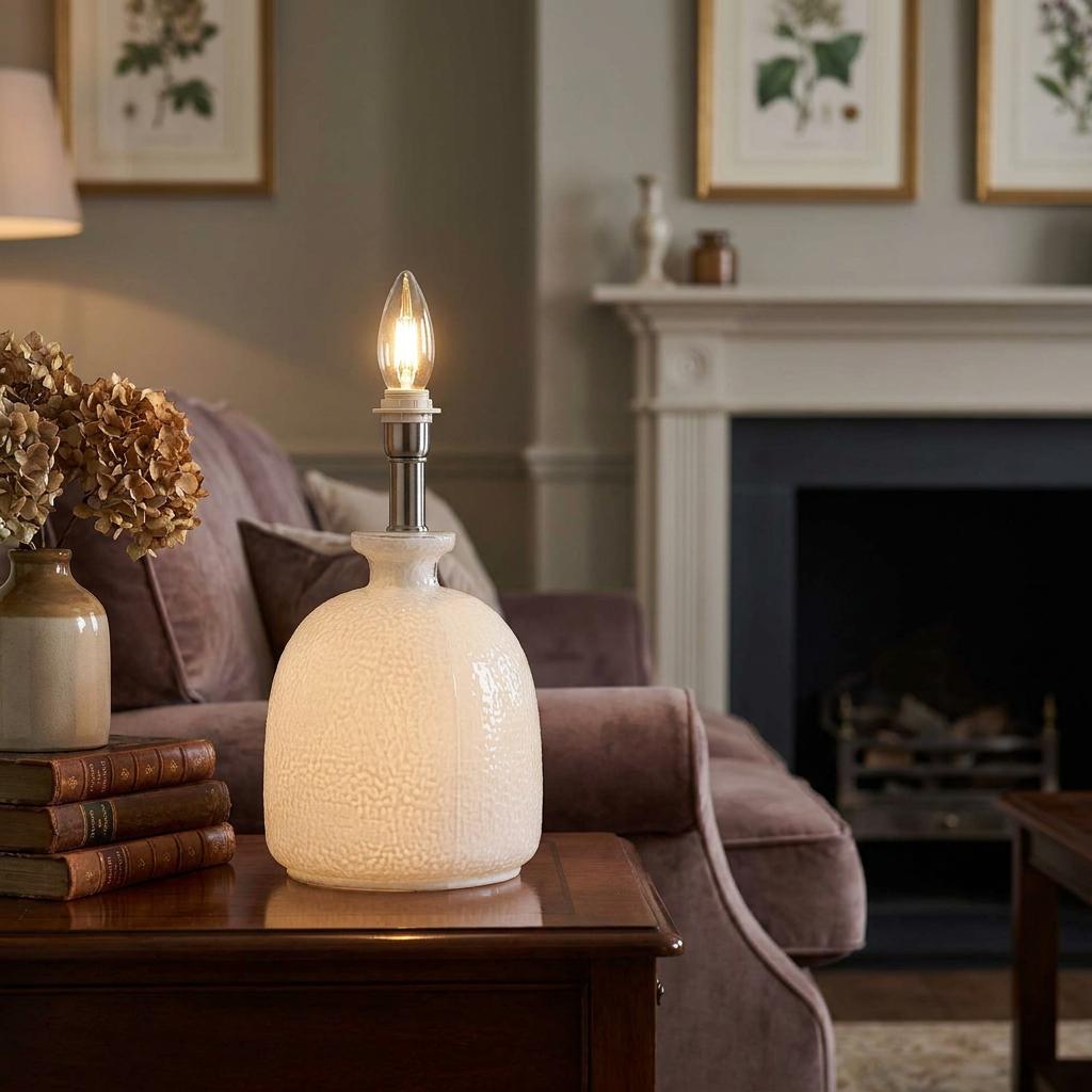 Textured white glass table lamp with a glowing candle bulb on a wooden side table in a cozy living room.