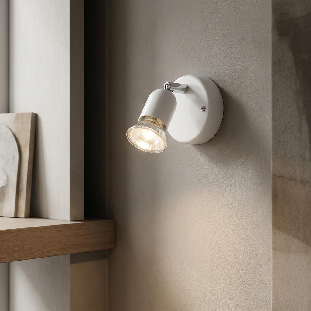 White single adjustable spotlight mounted on a wall, illuminated and casting a warm glow downwards.