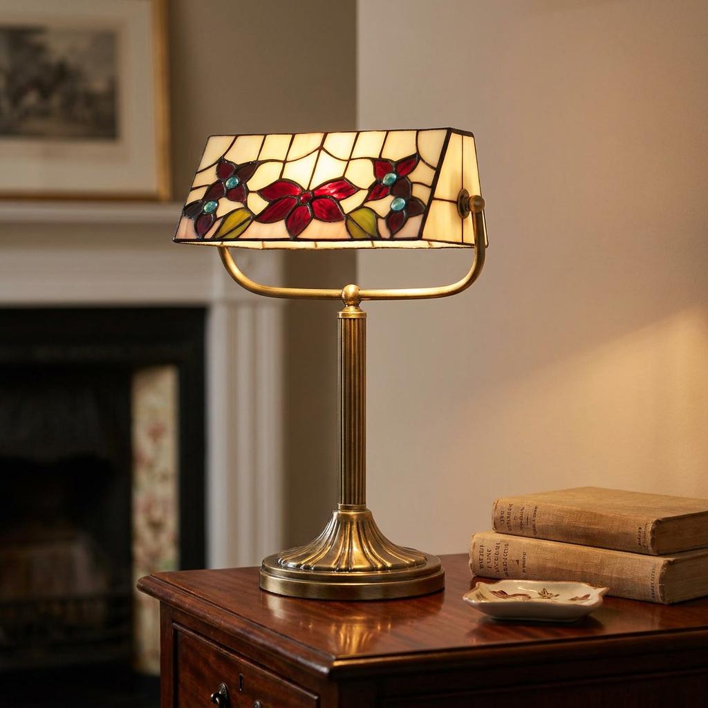 Tiffany-style bankers lamp with red floral stained-glass shade and brass base on a wooden desk.