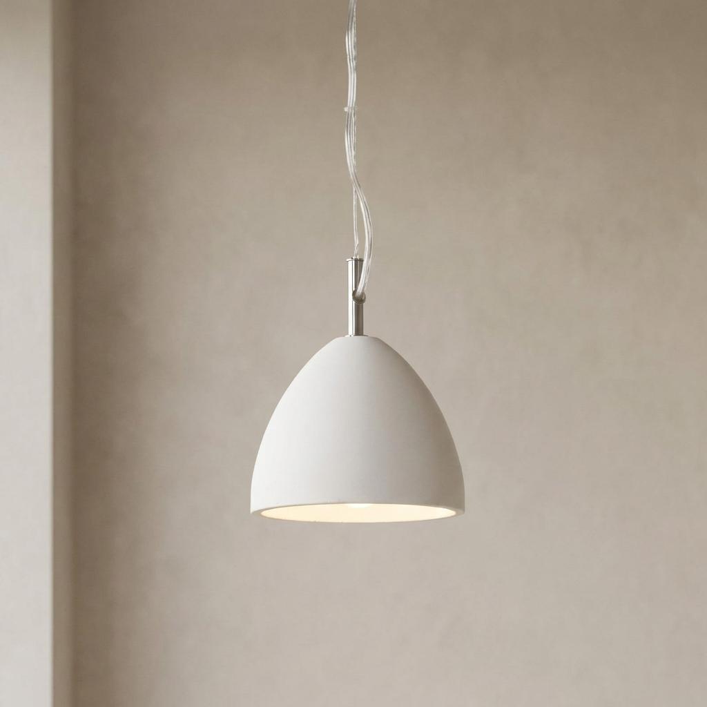 White concrete dome pendant light with a warm glow hanging against a textured neutral wall.