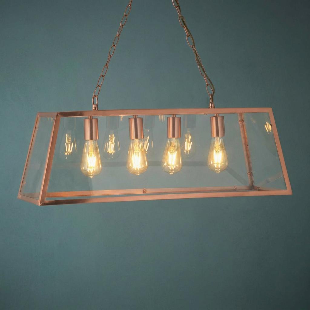 Rectangular copper and glass lantern pendant light with four glowing filament bulbs against a teal wall.