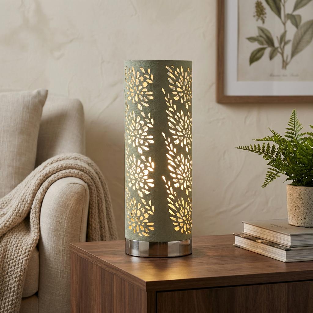 Sage green cylindrical table lamp with floral cutouts glowing on a wooden side table in a cozy living room.