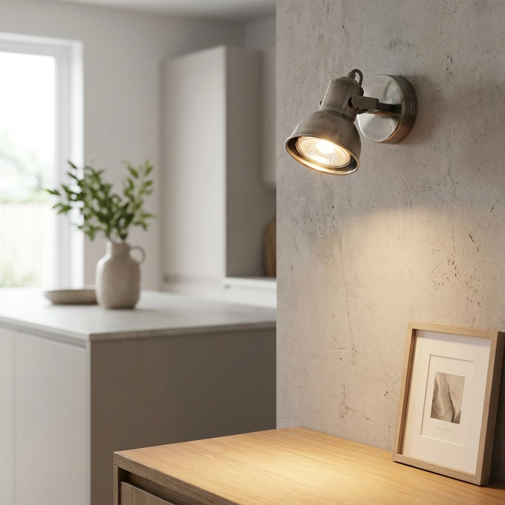 Antique chrome single spotlight mounted on a textured wall, illuminating a framed picture on a wooden surface.
