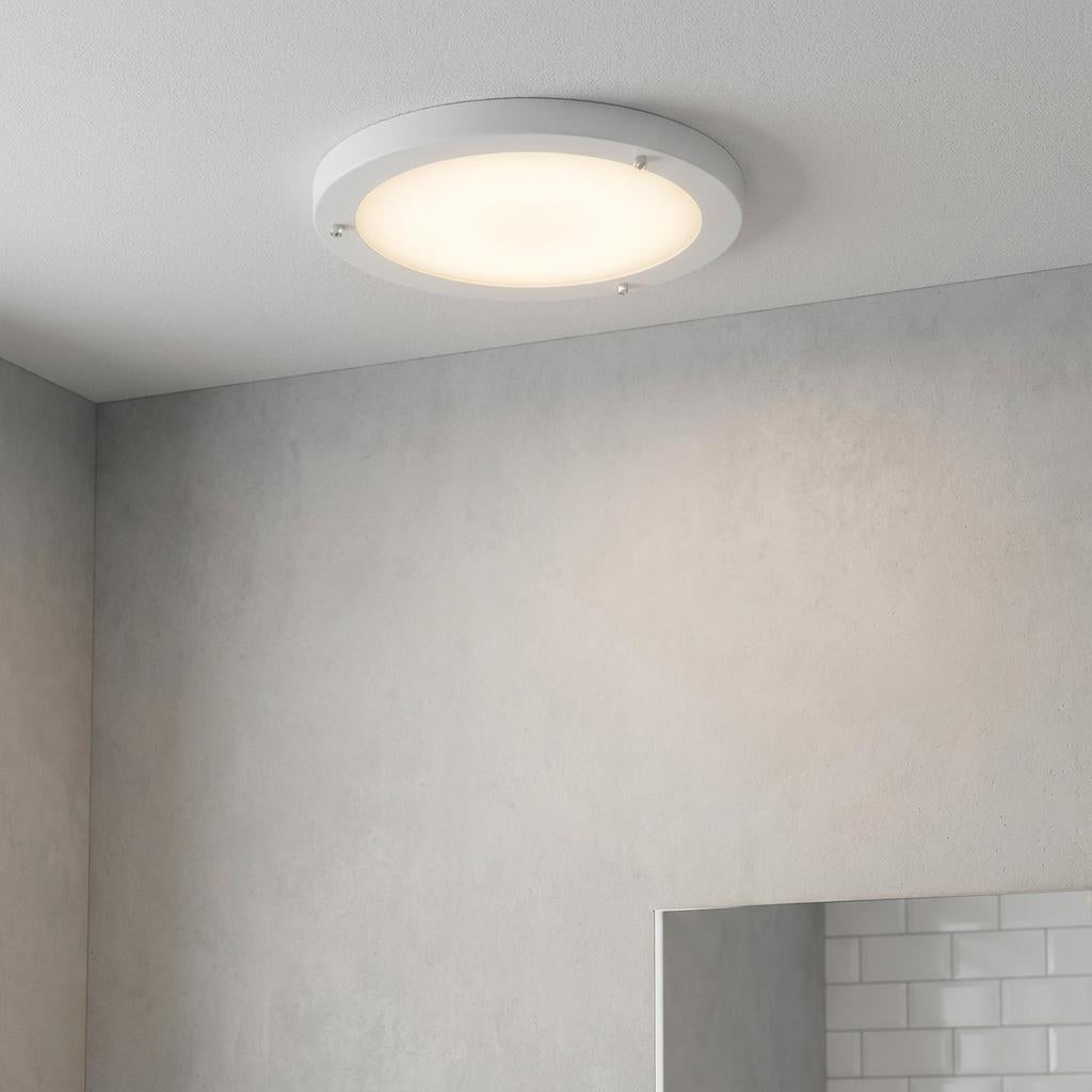 A circular white flush ceiling light with a warm glow mounted in a modern bathroom setting.