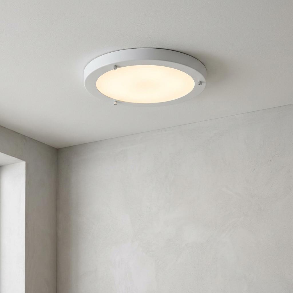Circular white flush bathroom ceiling light with a frosted diffuser emitting a warm glow against a white ceiling.