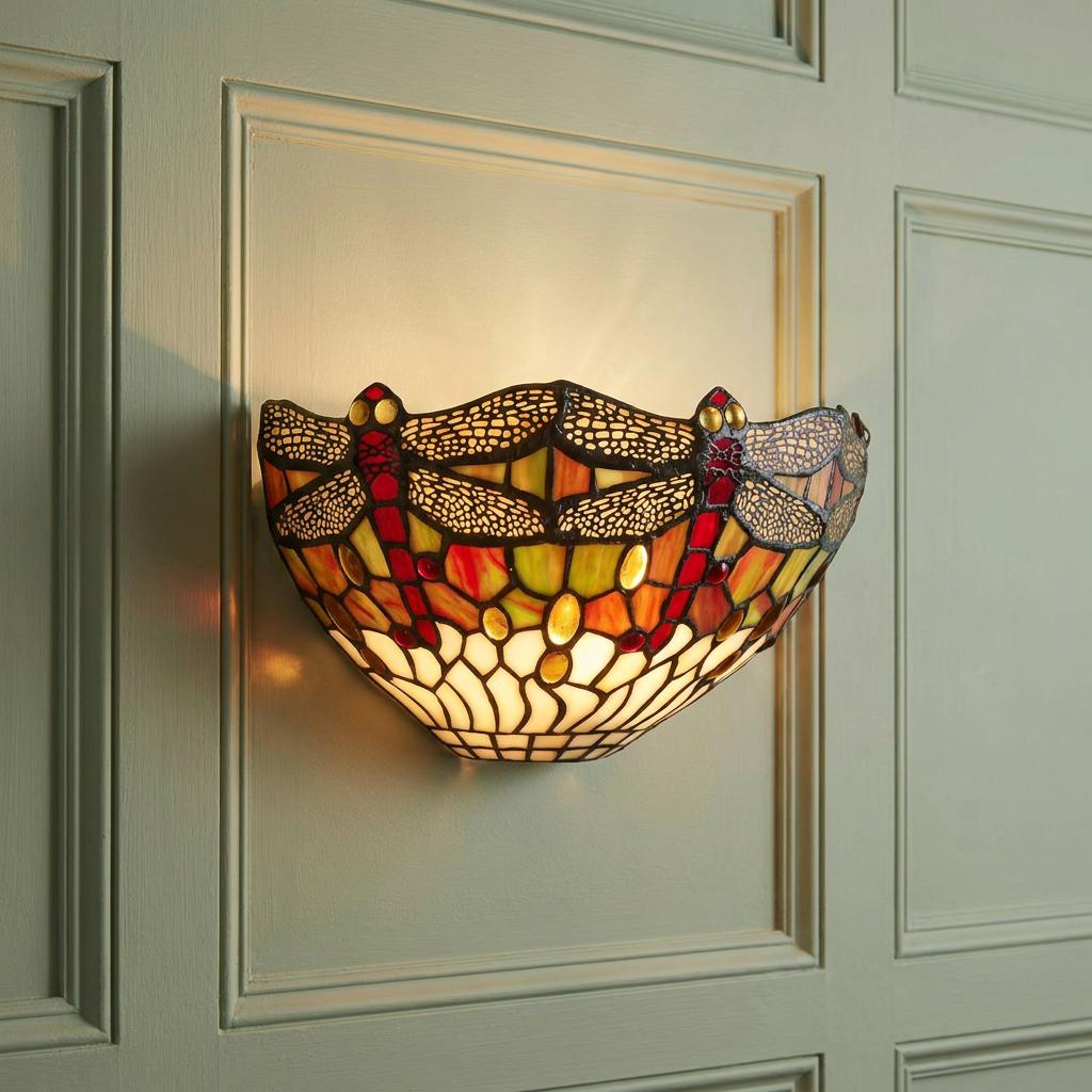 Lit Tiffany dragonfly wall lamp with red and amber stained glass on a light green paneled wall.