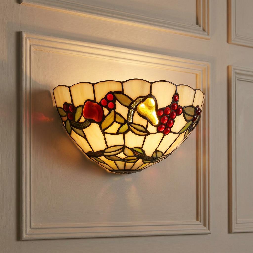 Lit Tiffany-style wall sconce with a stained-glass fruit motif mounted on a light-colored paneled wall.
