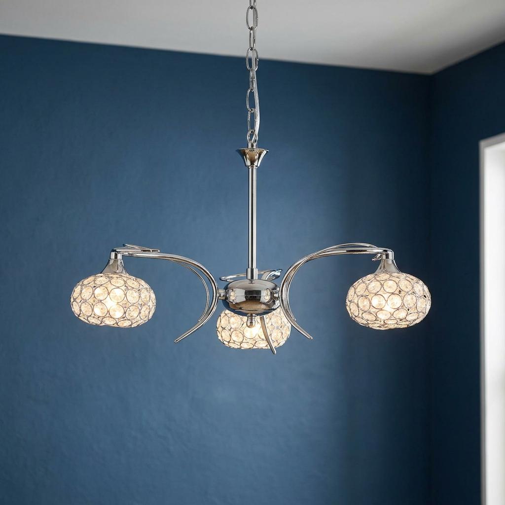 Three-light chrome chandelier with curved arms and crystal-patterned oval shades against a blue wall.