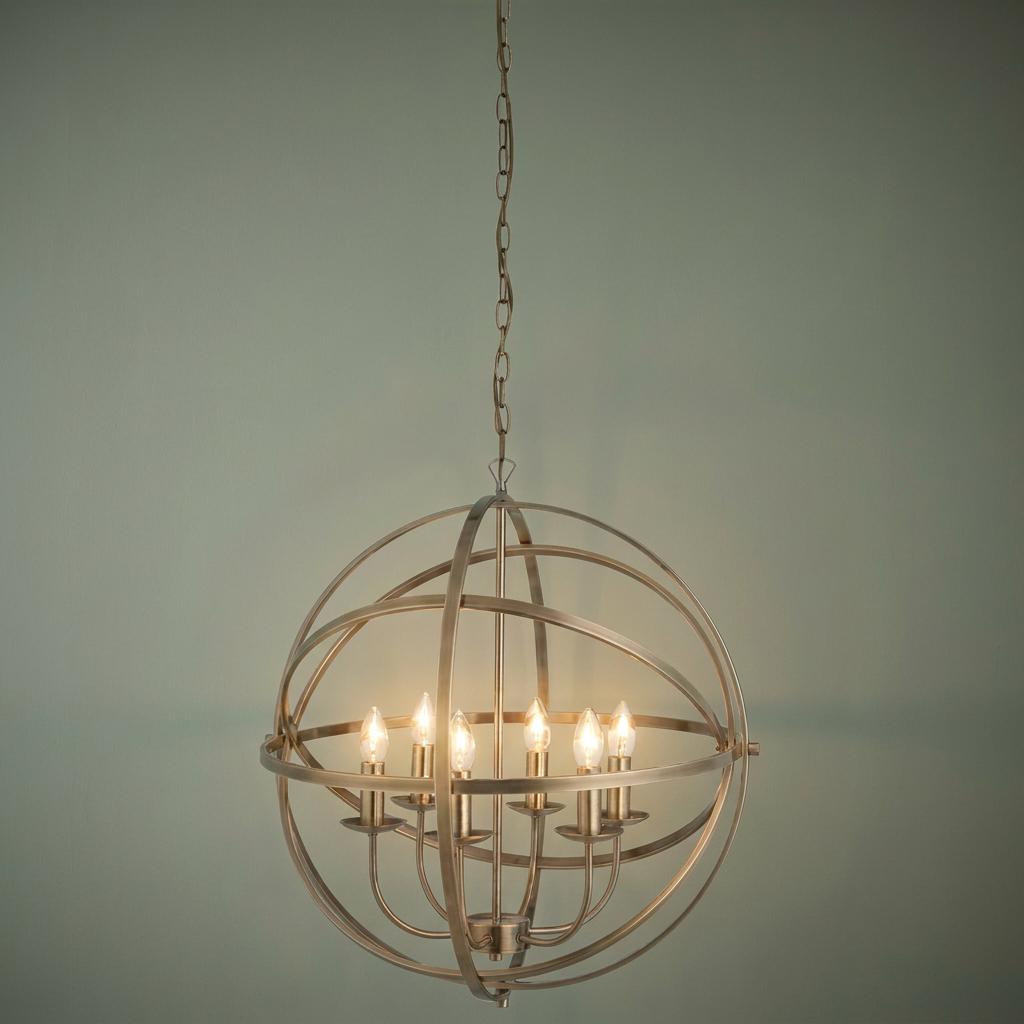 Orbit 6-light brass orb cage pendant chandelier with lit candle bulbs against a neutral wall.