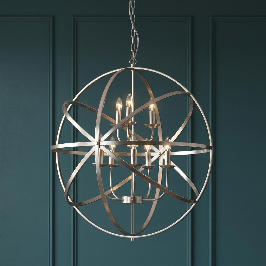 Satin silver orb chandelier with glowing candle lights hanging in front of a teal paneled wall.