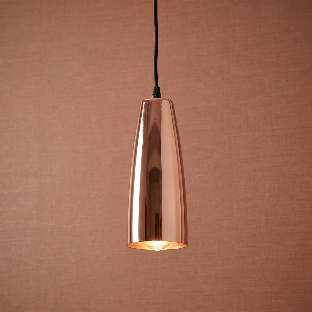 Polished copper cone-shaped pendant light hanging against a textured terracotta background.