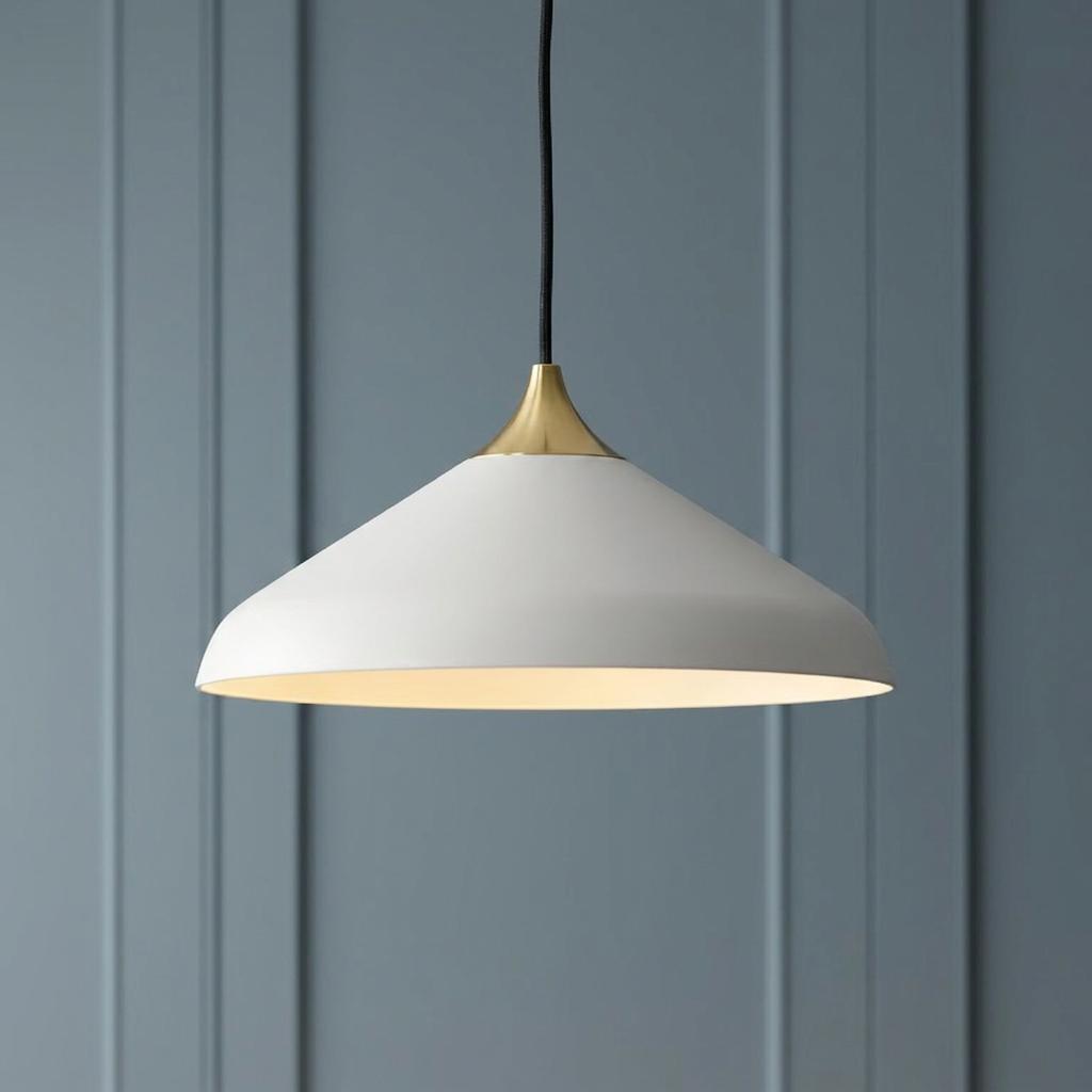 White coned industrial pendant light with a brass cap hanging against a blue paneled wall.